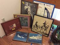 Seven framed art pieces arranged on the floor including panda, knights, aircraft, forest, bird and Hunter's Child prints.