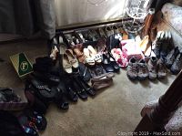 Wide view showing multiple pairs of men's and women's shoes arranged on carpet including boots, sandals, and casual shoes in various colors and styles.