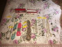 Full array of costume jewelry laid out on floral bedspread including necklaces, bracelets, earrings, some tagged or boxed, showing diversity of items and styles