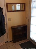 Wooden shelf with two shelves placed on floor below the mirror