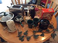 Wide image showing green cookware, a metallic toaster, hand mixer, crockpot, various kitchen accessories including mugs, paper towel holder, and box with baking pan.