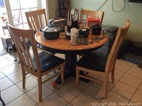 Full view of the round wood pedestal dining table with four matching chairs around it, showing the wood color and general condition.