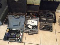 Overview photo showing multiple power tools in cases and some accessories arranged on floor tile.