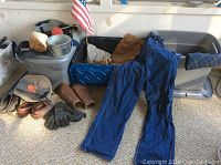 Overview of work clothes including denim overalls, leather calf protectors and storage bins containing additional clothing items.