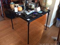 Full view of the lightweight metal folding card table with various items placed on top (not included in the lot).