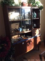 Full view of the Tollins Mid Century Modern china hutch with glass doors and wood lower cabinet, showing some wear and scratches. Contains decorative items not included.