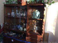 Wide view of wooden display cabinet containing Austrian crystal decanters, glassware, pottery, and other items arranged on shelves