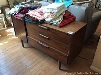 Full front view of walnut veneer buffet with linens on top and three drawers visible