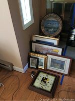 Photo showing stacked framed prints, decorative ceramic plate with wildlife design, vintage KORS clock with broken glass, and KORS accessories on floor.