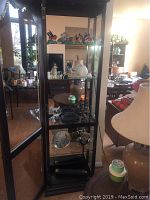 Glass front wooden display cabinet containing various collectible figurines, plates, and candlesticks including brass reindeer candle holders and panda figurine visible