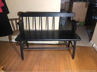 Front view of black wooden bench showing the seat, backrest with vertical spindles, armrests, and legs