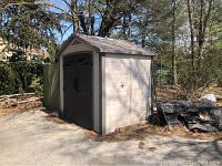Front-right angle view of tan resin shed against fence and yard.