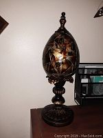 Front view of decorative egg statue on pedestal showing stained glass or mosaic pattern and ornate base.
