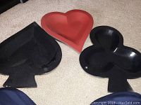 Three poker-themed plastic plates on a beige carpet, shaped as heart (red), spade (black), and club (black).