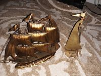 Close-up of two brass sail boat figurines on carpet, showing detailed multi-sail ship and smaller single sail figure.