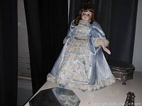 Front view of porcelain doll in blue satin dress with lace ruffles.