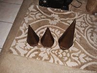 Three cone-shaped bass metal trees arranged on a patterned rug, showing their different sizes and solid cone shape.