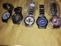 Five wristwatches featuring NFL team logos with metal bands, some wrapped in plastic.