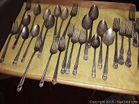 Multiple views of 1847 Rogers Bros silverware spread out on a wooden tray. Pieces include forks and spoons with decorative handles.