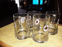 Four Warsteiner branded clear glass beer mugs with handles on a table, showing front and side logos.