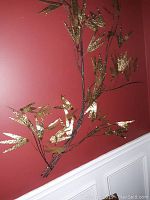 Two decorative artificial wall branches with gold metallic leaves against a red wall background, positioned vertically.