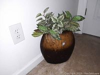 Front angled view of the wooden flower vase with attached artificial plant, against a white wall and carpeted floor.