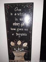 Photo of rectangular wooden wall plaque with floral painting and inspirational quote about love and fairy tales.