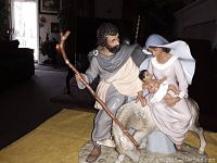 Figurine depicting Joseph standing with staff, Mary seated holding baby Jesus, and a lamb at their feet, shown from front angle.