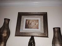 Framed flower print wall picture centered on wall, flanked by two decorative large vases with a rustic metallic finish and textured look