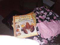Cookbook and floral apron laid on a surface, showing cover of book and full apron with pocket.