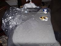 Five Missouri team shirts folded with tags visible, showing team tiger logo on front.