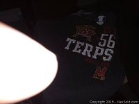 Photo of a Maryland Terps dark gray T-shirt with front graphics showing '56' and 'TERPS' with the Maryland 'M' and terrapin mascot.
