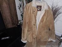 Front view of tan men's shearling jacket with button closure and pockets.