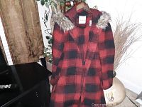 Red and black plaid coat with a faux fur trimmed hood hanging on a hanger.