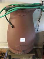 Full front view of terra cotta color rain collection barrel with green hoses draped on top