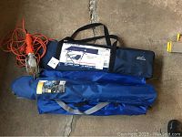 Photo of two packed folding camp chairs, one folding camp cot, and an orange hanging work lamp with cage.