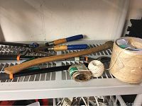 Garden tools including loppers, wooden handled hoe, and two twines on a shelf