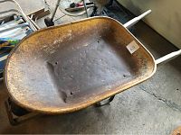 Top view of rusty metal body of wheelbarrow showing worn condition with white wooden handles