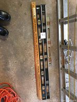 Two spirit levels and two wooden yardsticks laid on the floor, showing their full length with some branding and tool details visible.