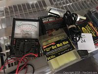 Photo showing two glue guns with power cords, two packs of hot melt glue sticks, an analog voltage meter, and two packs of staples.