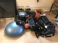 Full view of BOSU balance trainer, basketballs, water bags, suspension trainer straps, and other workout gear arranged on floor.