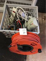 Plastic basket filled with multiple surge protectors, power strips, adapters and long orange extension cord on a black reel