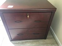 Front view of the dark wood-finish lateral file cabinet showing two drawers, black handles, and a lock with keys inserted.