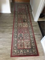 Long narrow rectangular area rug runner with repeated floral medallion blocks in red, beige, and black with intricate border