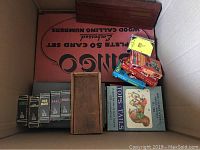 Top-down photo of various board and card games inside a box, showing Bingo set, several boxed card games, wooden holders, and vintage puzzle boxes.