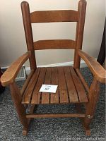 Wooden child's rocker with a slatted seat, showing wear and patina.
