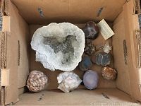Top down view of assorted rocks and minerals in banker box including large white quartz geode and various agate and nodule specimens.
