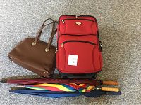 Overview of red expandable suitcase, brown handbag, and three umbrellas on carpet.