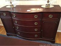 Full frontal view of antique mahogany buffet showing six drawers and two cabinet doors with brass handles on wooden floor.