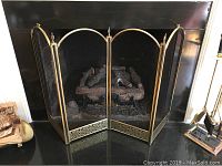 Brass four-panel fireplace screen with mesh panels in front of a fireplace.